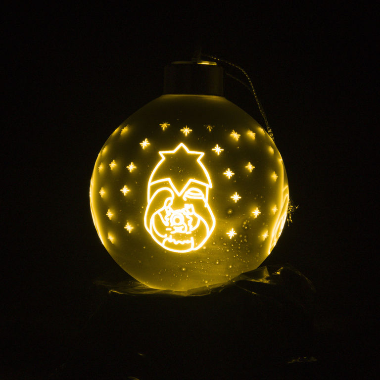 Boule en verre argentée lumineuse LED avec décor nativité enfantine, à suspendre Ø 8 cm, livrée en boîte.